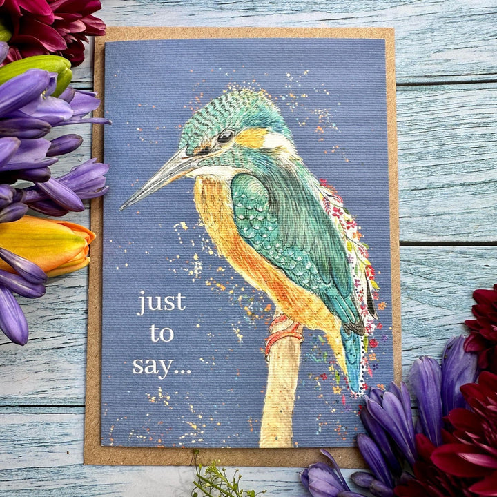 A square greeting card featuring a painted kingfisher on a blue-gray background with the text &